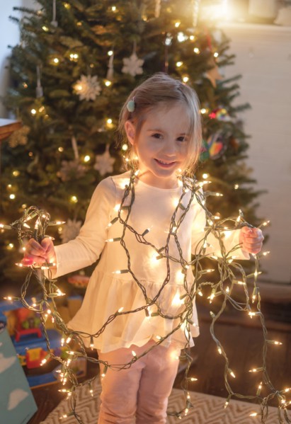 Little girl (4-5) wrapped with christmas lights in living room