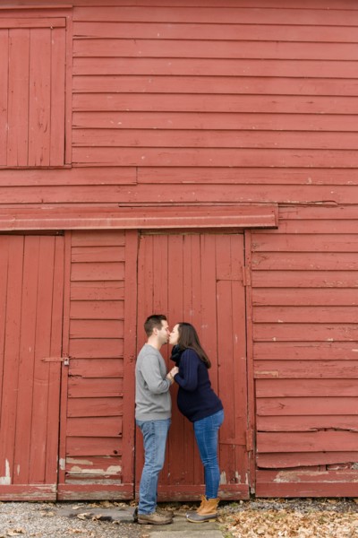 Couple kissing in front of red barn