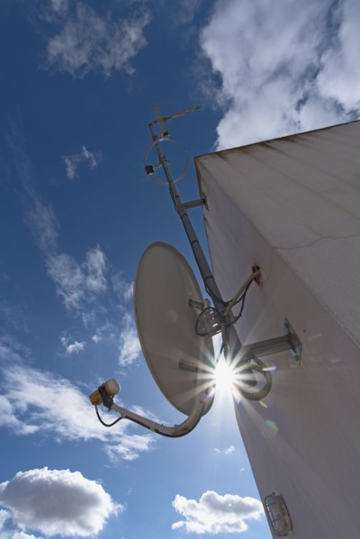 Sun shining through space between satellite dish and facade