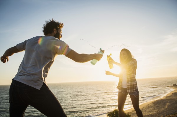 Couple having water fight on beach at sunset