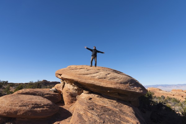 Man with arms outstretched on rock in Arches National Park, Utah, USA