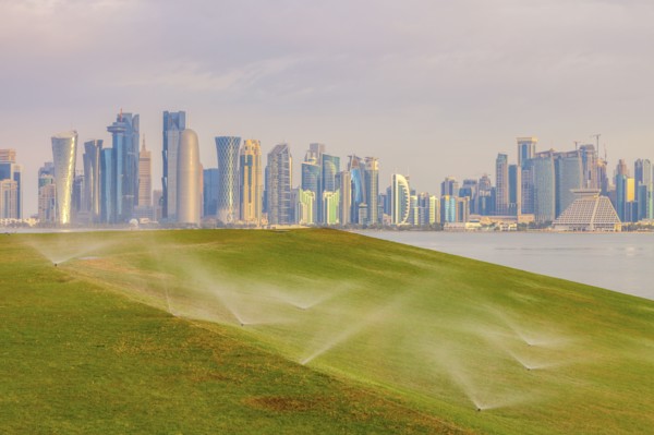 Sprinkler system on lawn by skyline of Doha, Qatar