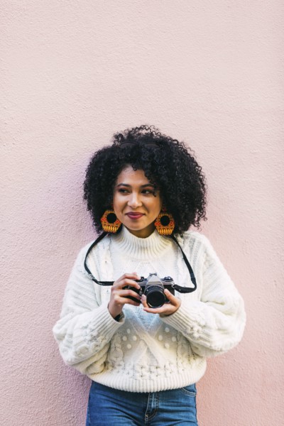 Young woman holding camera against pink wall