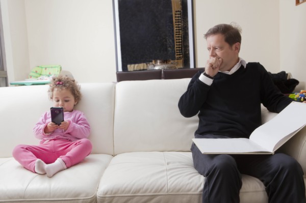 Girl using smart phone as her father reads book