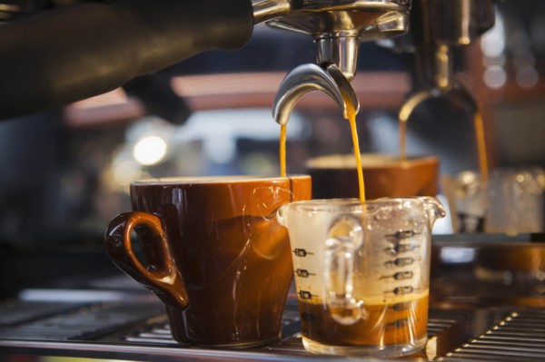 Coffee pouring from portafilter into coffee cup and beaker