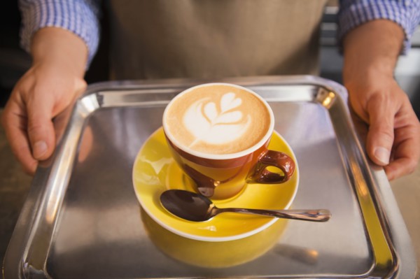 Barista holding yellow cup of coffee on tray