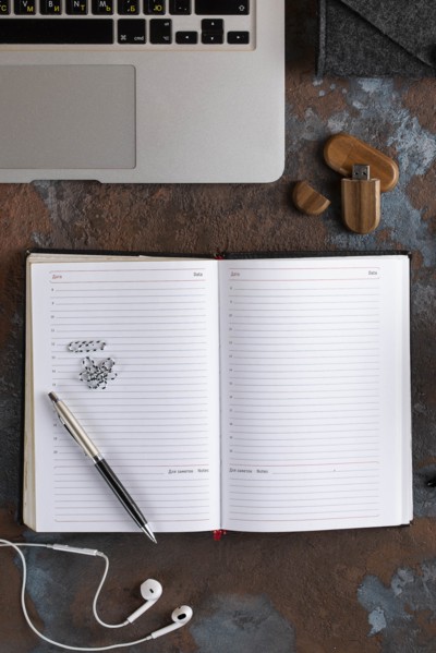 Open notebook by laptop with earbuds and USB stick
