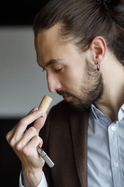 Young man smelling wine on cork at tasting