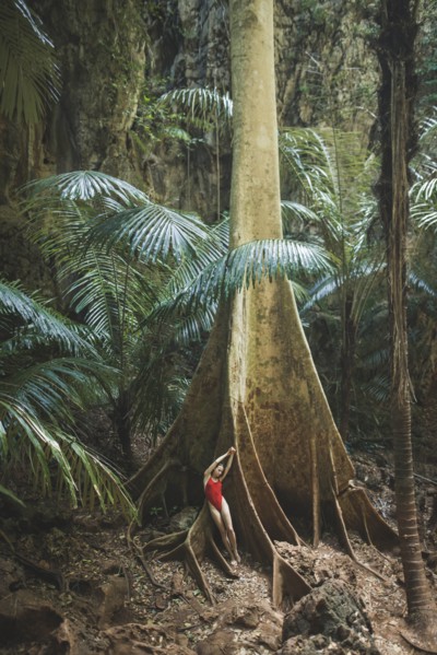 Young woman in swimsuit leaning on large tree in Krabi, Thailand