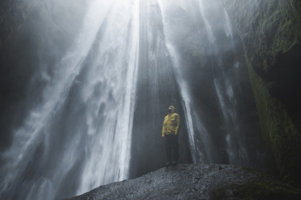 Man wearing yellow raincoat by Seljalandsfoss waterfall in Iceland