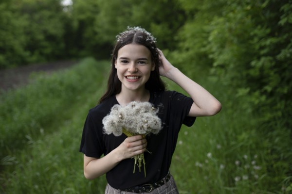 Smiling teenage girl holding dandelions in a field
