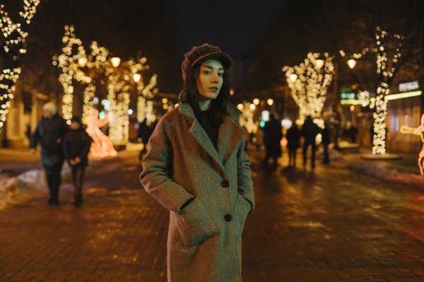 Young woman wearing coat on street at night with fairy lights
