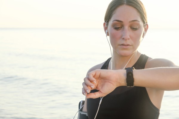 Woman wearing headphones checking wrist watch on beach