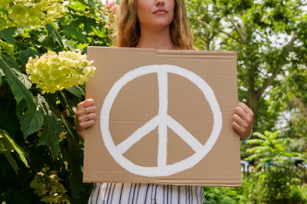 Woman holding peace symbol by trees