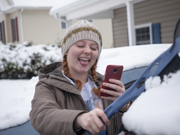 Girl taking selfie while brushing snow off of car