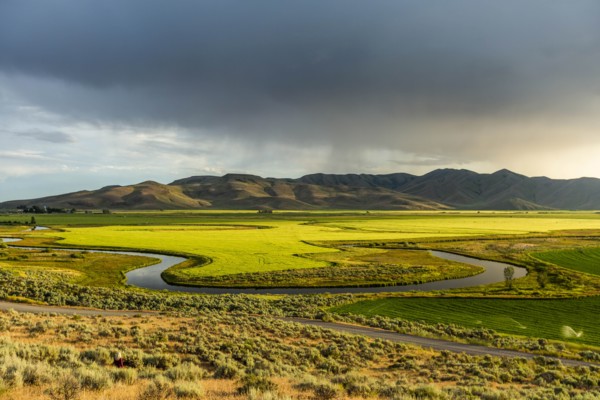 River through fields by hills in Picabo, Idaho, USA