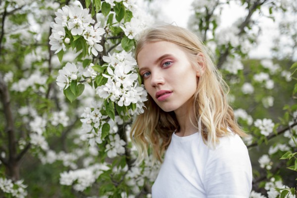 Blond haired young woman among white blossoms