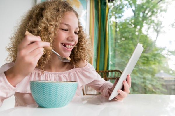 Smiling girl eating breakfast using tablet