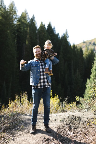Father carrying his daughter on his shoulders by forest