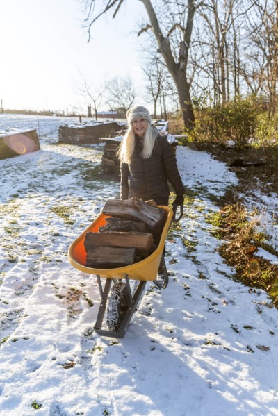 Woman holding wheelbarrow with logs in snow
