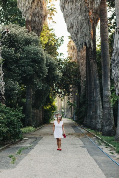 Woman in white dress walking on footpath between palm trees