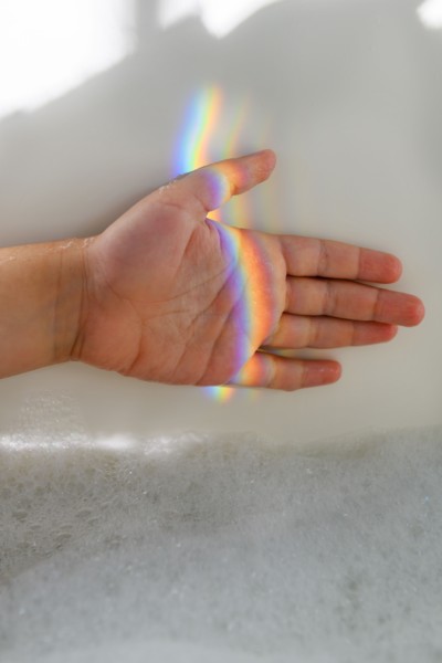 Girl's hand in rainbow light beam in bubble bath