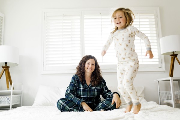 Girl jumping on bed and her smiling mother
