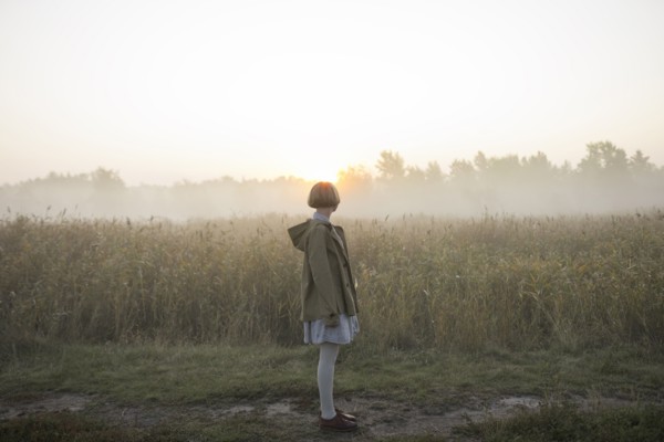 young woman by field of long grass at sunset