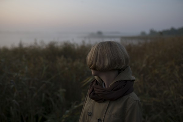young woman in field by lake at sunset
