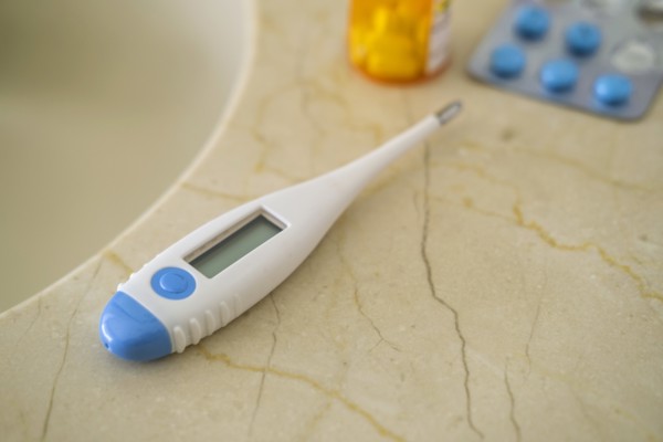 Thermometer and pills on stone surface