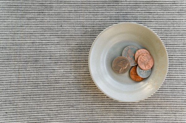 Bowl with small pile of coins on striped background