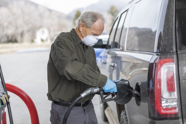 Man wearing surgical gloves and mask refueling car at gas station