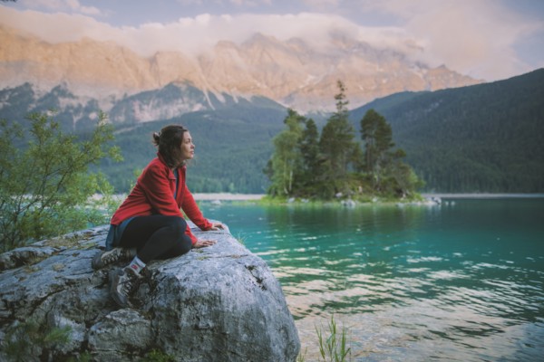 Germany, Bavaria, Eibsee, Young woman sitting on rock and looking at scenic view by Eibsee lake in Bavarian Alps