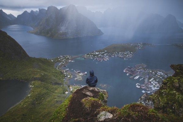 Norway, Lofoten Islands, Reine, Man looking at fjord from Reinebringen mountain during rain