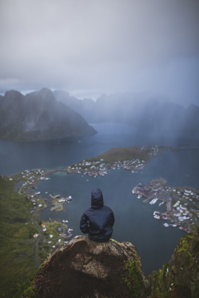 Norway, Lofoten Islands, Reine, Man looking at fjord from Reinebringen mountain during rain