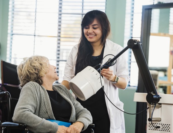 Smiling doctor holding machine by senior woman