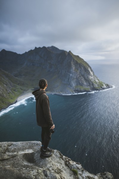 Man holding camera on cliff at Ryten mountain in Lofoten Islands, Norway