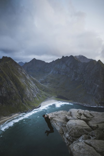Man hanging on cliff at Ryten mountain in Lofoten Islands, Norway