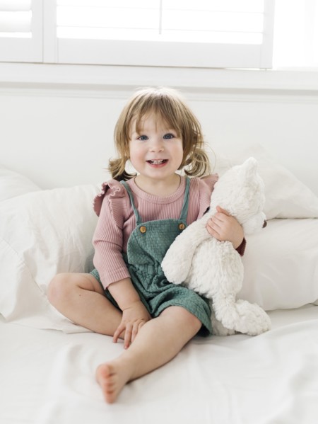 Girl (2-3) sitting on bed with teddy bear