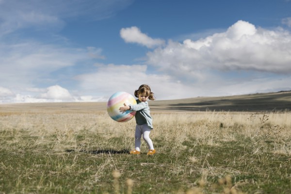 Girl (2-3) holding ball in open field
