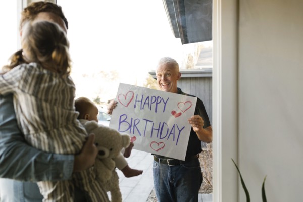 Grandfather showing happy birthday message to family with grandchildren (2-3 months, 2-3) through window