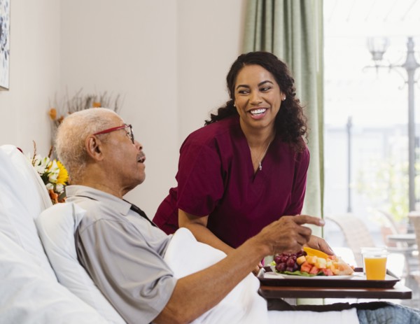 Nurse bringing healthy meal to senior man in bed