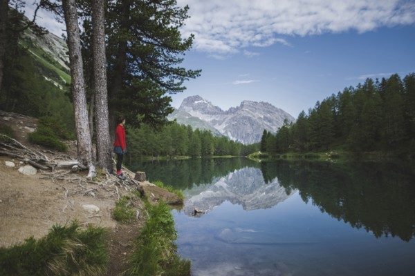 Switzerland, Bravuogn, Palpuognasee, Young woman resting on bench near Palpuognasee lake in Swiss Alps