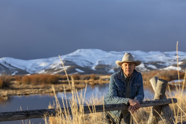 USA, Idaho, Sun Valley, Senior man in cowboy hat leaning against fence
