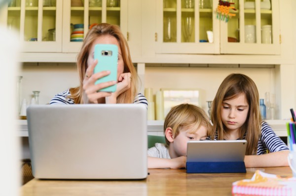 Woman holding smart phone in front of laptop while boy (4-5) and girl (6-7) using digital tablet