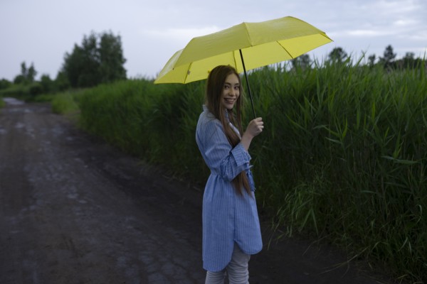 Russia, Omsk, Portrait of young woman with umbrella on dirt road