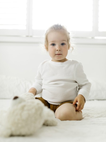 Smiling toddler girl sitting on bed with teddy bear toy