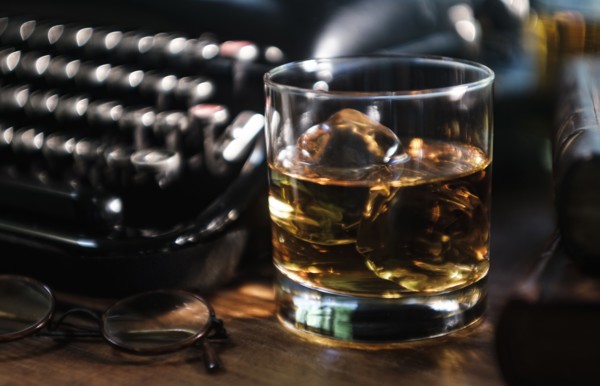 Whiskey glass next to typewriter on desk