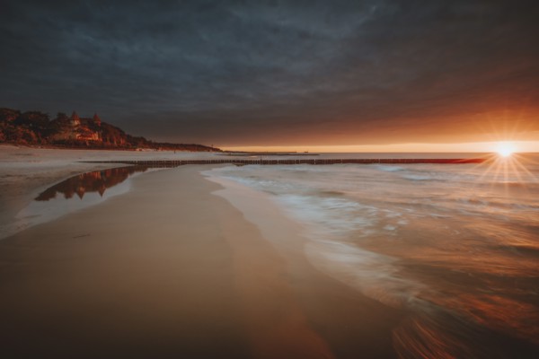 Poland, Pomerania, Leba, Baltic Sea coastline with distant town at sunset