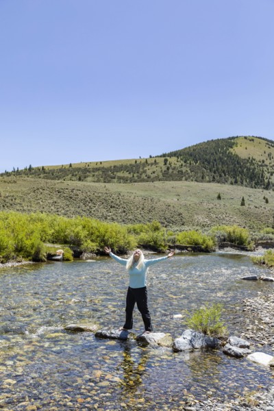 USA, Idaho, Sun Valley, Woman with arms raised standing on rocks in river